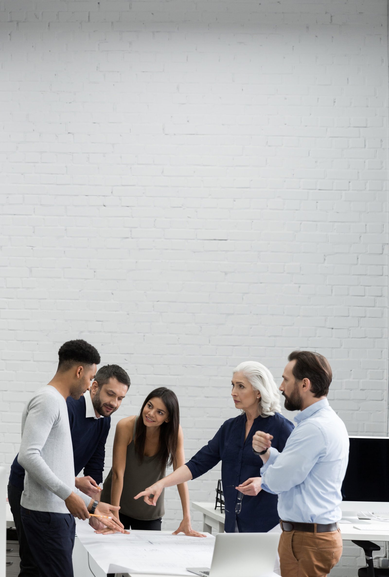 Group of serious business people in smart casual wear having a brainstorm meeting while standing at the office